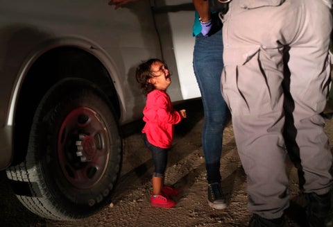 Una niña mirando a un oficial estadounidense tras ser separada de su familia en la frontera