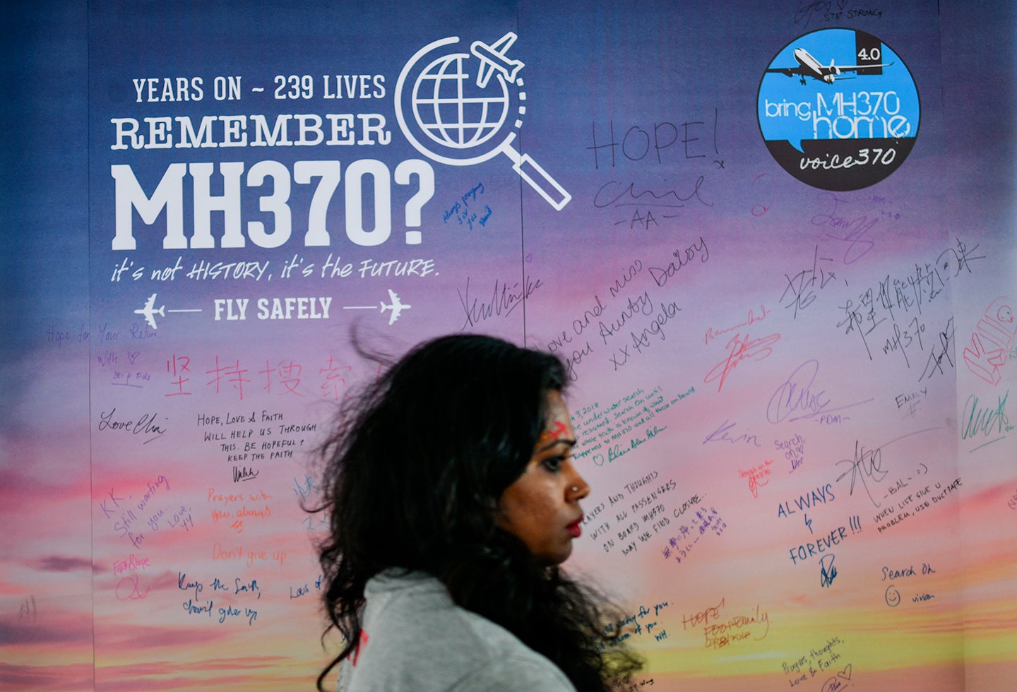 Una mujer camina en Kuala Lumpur (Malasia) mientras de fondo se observa un afiche que da cuenta de la desaparición del vuelo de Malaysia Airlines en 2014
