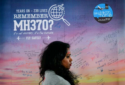 Una mujer camina en Kuala Lumpur (Malasia) mientras de fondo se observa un afiche que da cuenta de la desaparición del vuelo de Malaysia Airlines en 2014