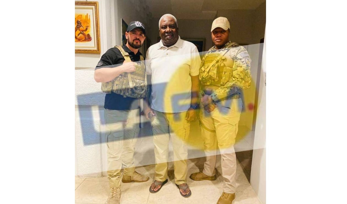 Emanuel Sanon viste una camiseta blanca y posa junto a dos militares