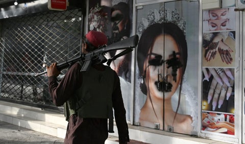 Talibán transita en calle de Afganistán frente a imagen de una mujer desfigurada con pintura.