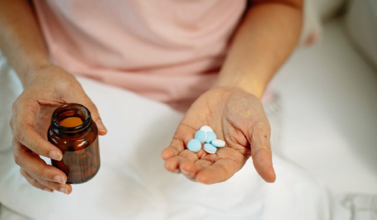 Una mujer con medicinas y un vaso de agua.