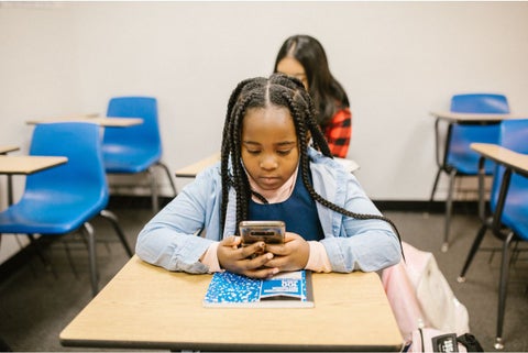 Niña con celular dentro de una aula de clases