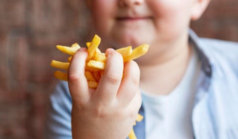 Niño con obesidad, come papas fritas