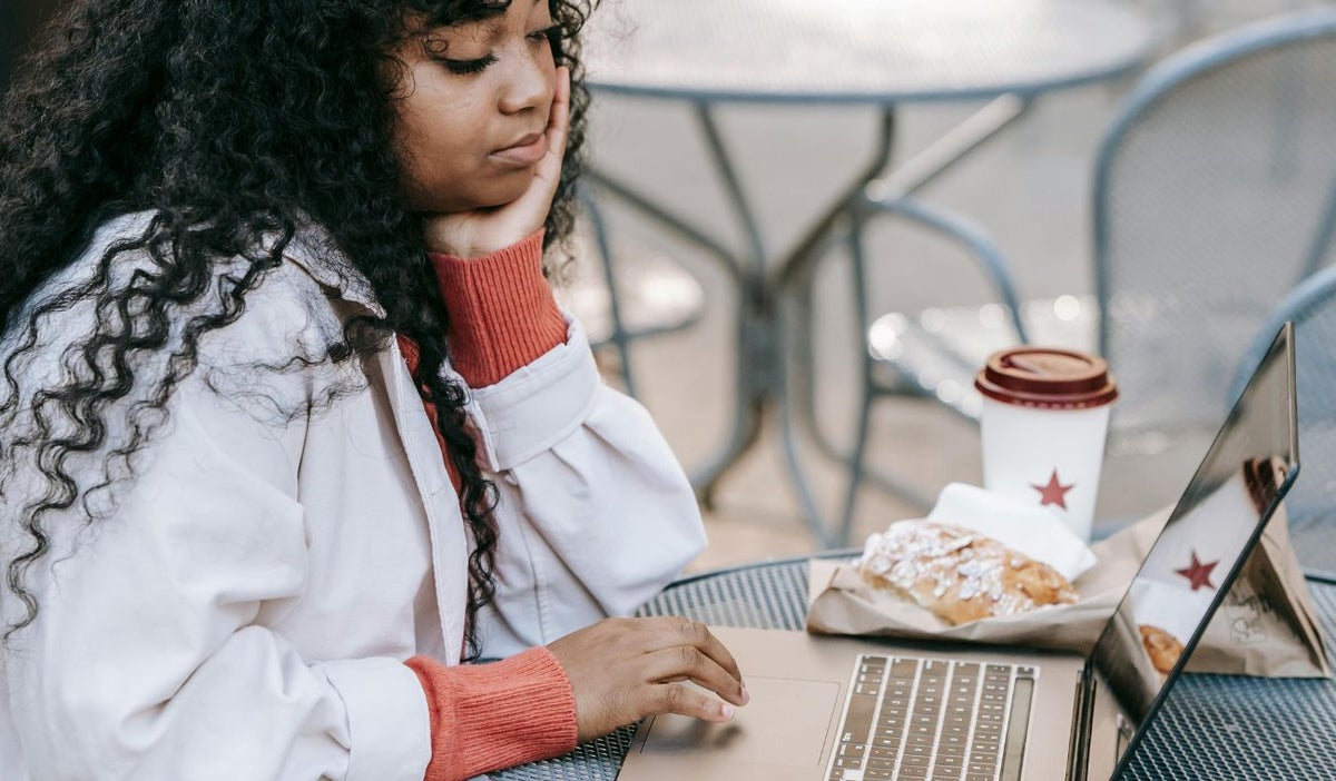 Una mujer comiendo y con un computador en la mesa