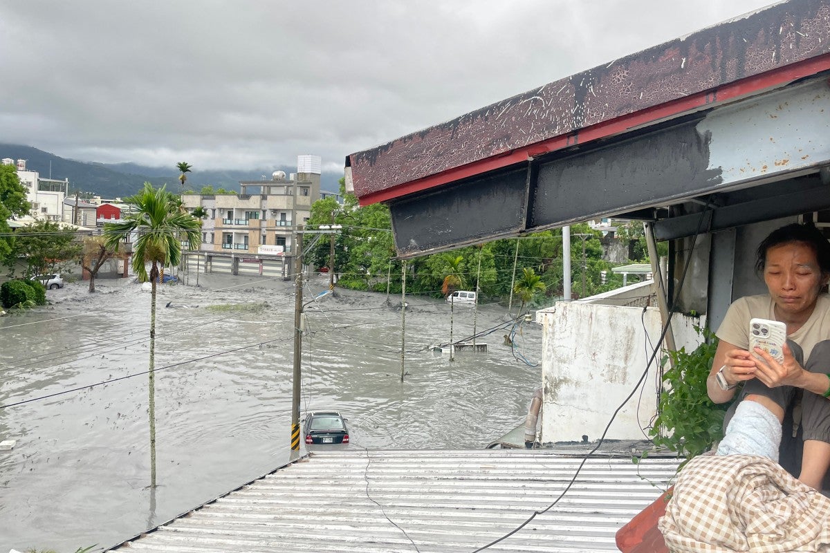 Una residente utiliza su teléfono móvil sentada en el tejado de una casa, mientras el agua de una presa reventada por un deslizamiento de tierra se desborda e inunda la zona de Hualien el 23 de septiembre de 2025, como consecuencia de las fuertes lluvias provocadas por el supertifón Ragasa.