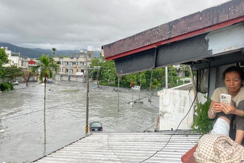 Una residente utiliza su teléfono móvil sentada en el tejado de una casa, mientras el agua de una presa reventada por un deslizamiento de tierra se desborda e inunda la zona de Hualien el 23 de septiembre de 2025, como consecuencia de las fuertes lluvias provocadas por el supertifón Ragasa.