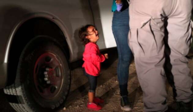 Una niña mirando a un oficial estadounidense tras ser separada de su familia en la frontera
