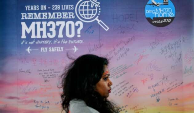 Una mujer camina en Kuala Lumpur (Malasia) mientras de fondo se observa un afiche que da cuenta de la desaparición del vuelo de Malaysia Airlines en 2014