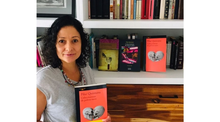 Pilar Quintana con uno de sus libros en sus manos y una biblioteca detrás de ella