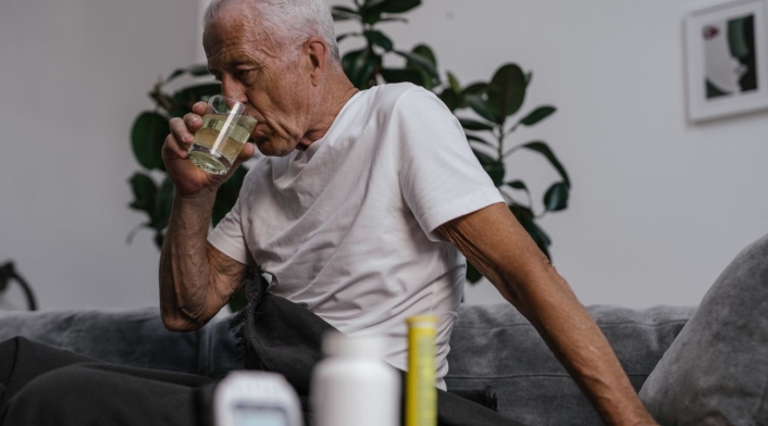 Anciano Anciano tomando algo y con medicamentos a su lado