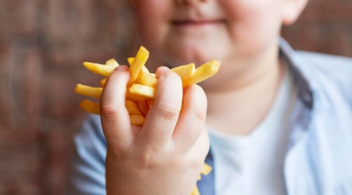 Cuántos años de vida pierden los niños con sobrepeso u obesidad Niño con obesidad, come papas fritas
