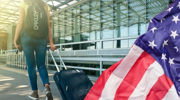 Nuevas reglas para el equipaje de mano para Estados Unidos Una mujer con dos maletas y la bandera de Estados Unidos