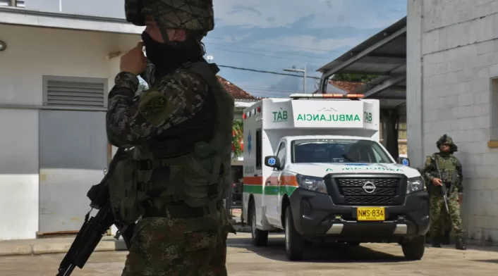 Un soldado hace guardia en Arauca mientras al fondo se ve una ambulancia que transporta a otro militar herido.