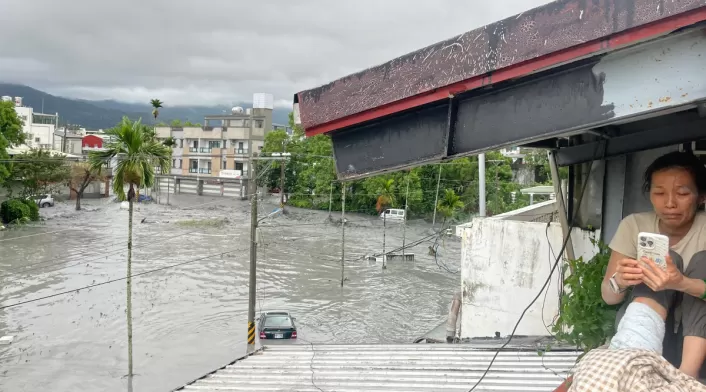 Una residente utiliza su teléfono móvil sentada en el tejado de una casa, mientras el agua de una presa reventada por un deslizamiento de tierra se desborda e inunda la zona de Hualien el 23 de septiembre de 2025, como consecuencia de las fuertes lluvias provocadas por el supertifón Ragasa.
