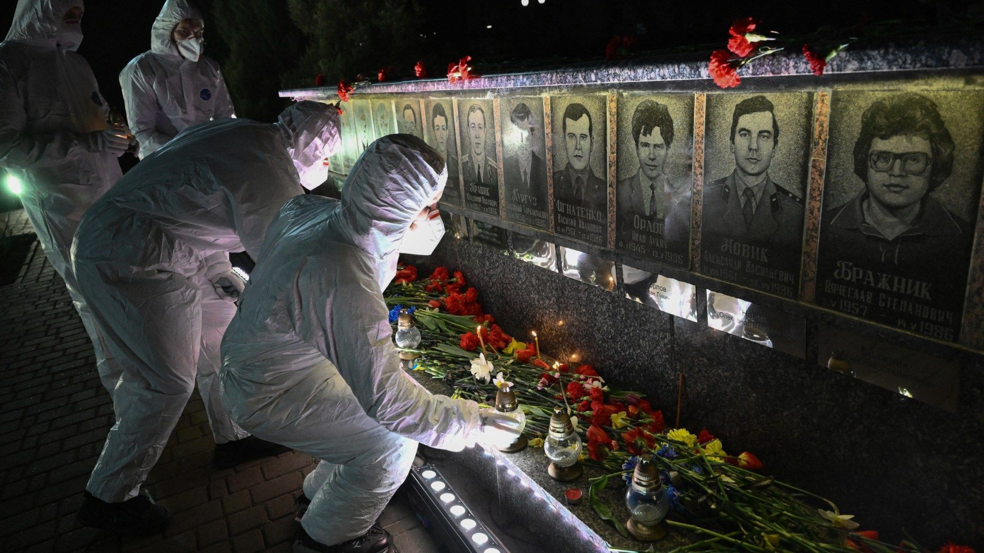 Participantes vestidos con trajes blancos de protección (hazmat), representando a los liquidadores, colocan velas frente a un monumento en memoria de las víctimas de Chernóbil, durante una ceremonia conmemorativa por el 40 aniversario de la explosión en la central nuclear de Chernóbil, el peor desastre nuclear civil de la historia, en la ciudad de Slavutych.