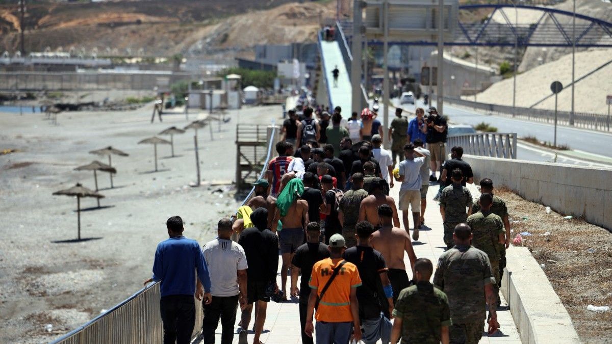 Un grupo de migrantes se acerca al puesto fronterizo para regresar a Marruecos, escoltados por soldados de infantería españoles, en el enclave español de Ceuta
