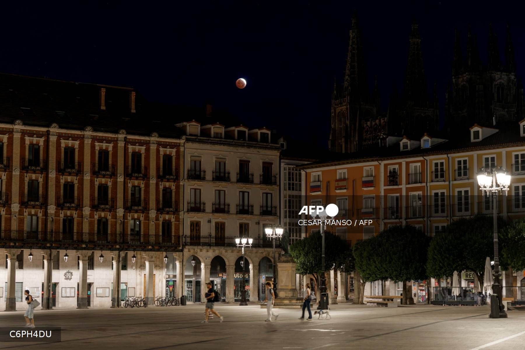 Unos peatones caminan por la Plaza Mayor de Burgos, en el norte de España, durante la noche del 27 al 28 de agosto de 2026, mientras se observa la Luna dentro de la umbra terrestre durante un eclipse lunar parcial.