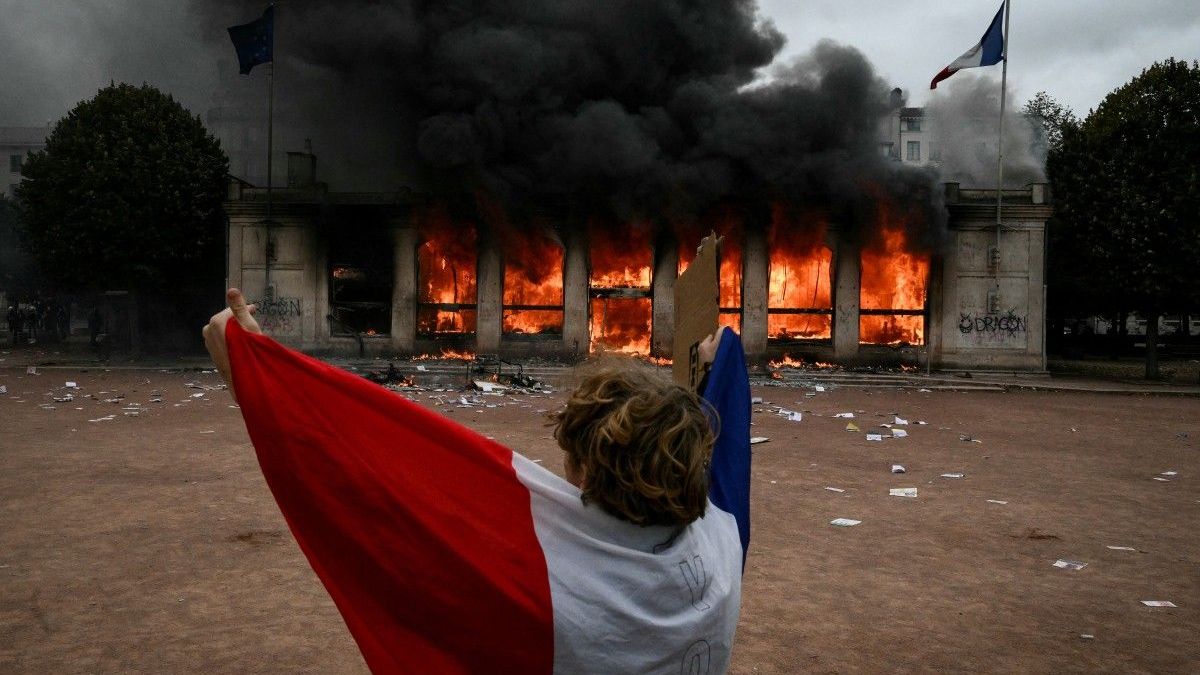Un manifestante envuelto en la bandera francesa se encuentra frente a la oficina de turismo de Lyon