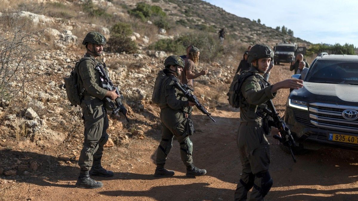 Soldados israelíes observan la escena mientras colonos israelíes se congregan y agricultores palestinos cosechan sus olivos en la aldea de Deir Abu Mashal, en la Cisjordania ocupada por Israel